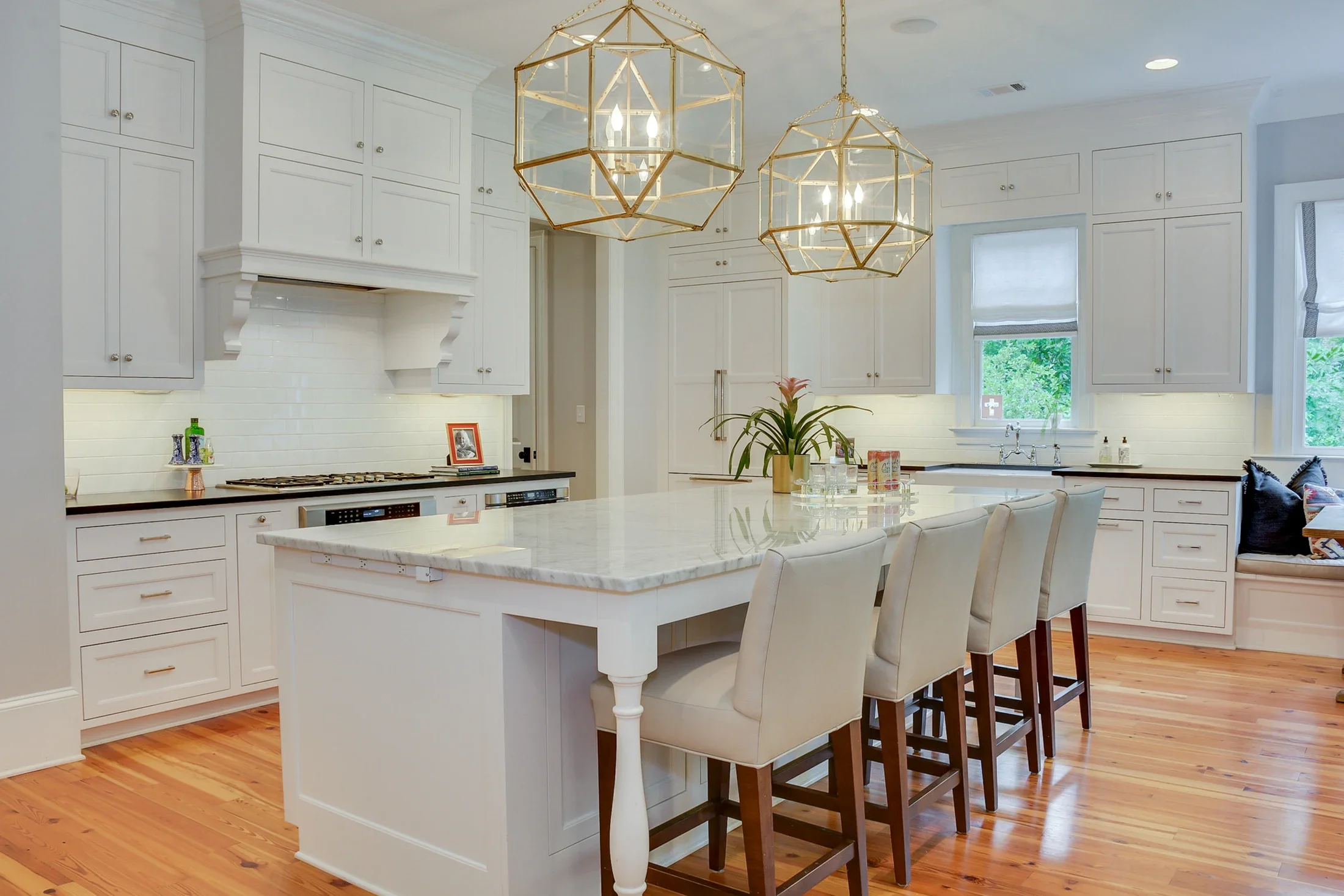 A spacious white kitchen with brass lantern pendants and a long island
