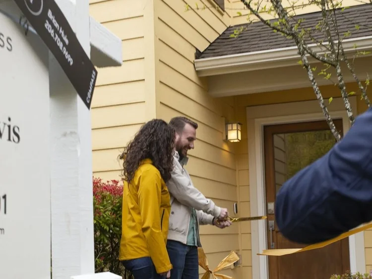 New homeowners cutting a ribbon at their front door on closing day