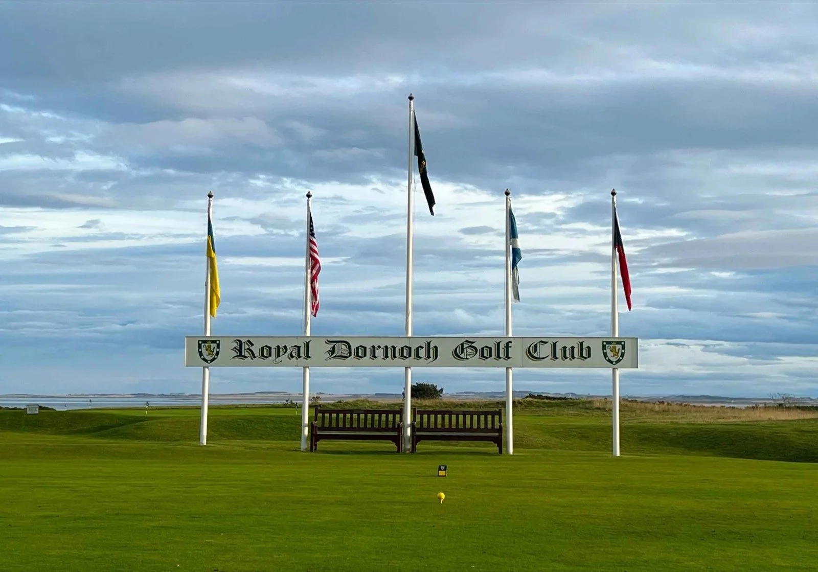 The Royal Dornoch Golf Club sign and flags above the first tee, with the Dornoch Firth beyond