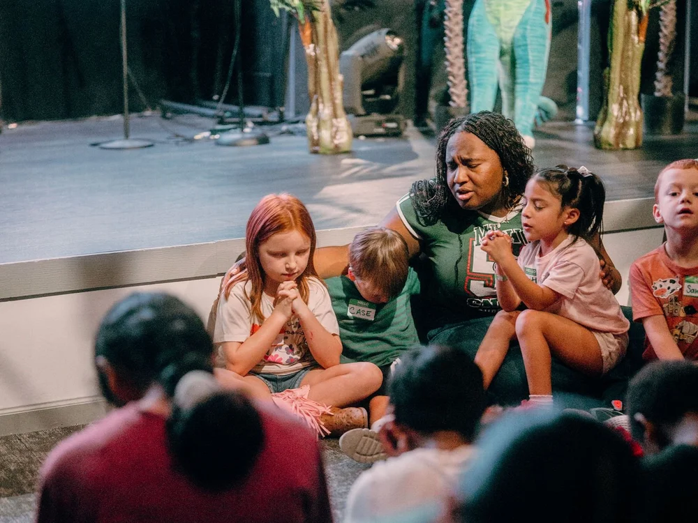 A leader sitting with a group of young kids as they pray together