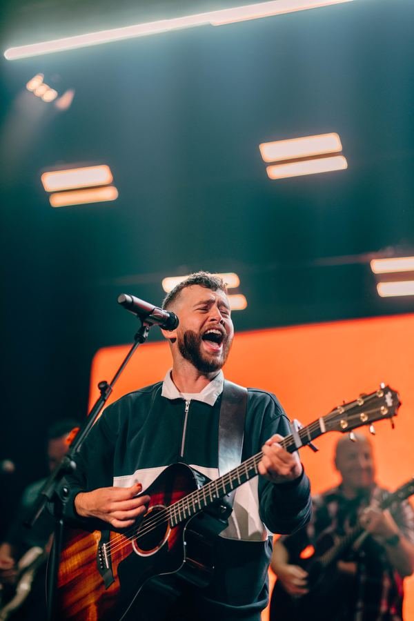 A worship leader singing and playing guitar on stage
