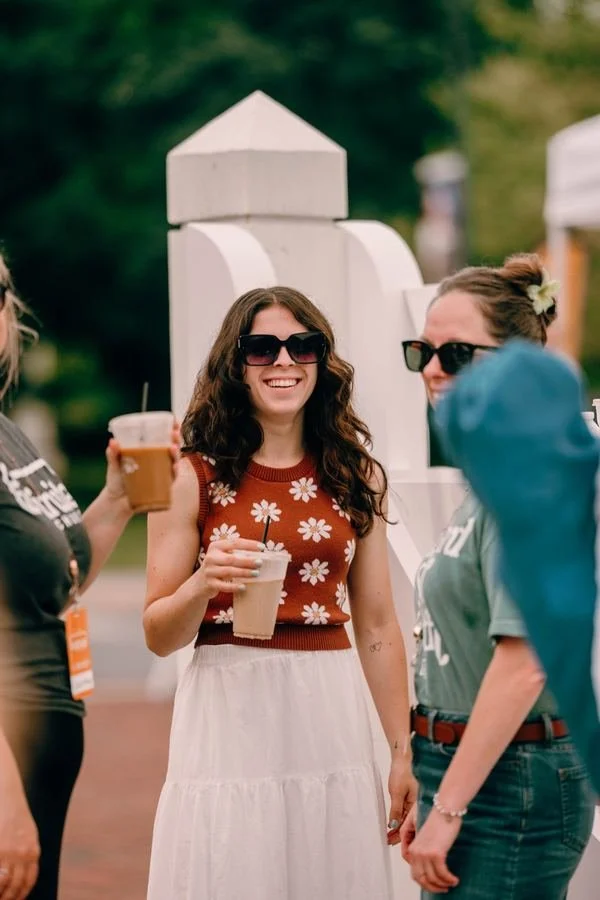 A woman smiling with an iced coffee among friends outside