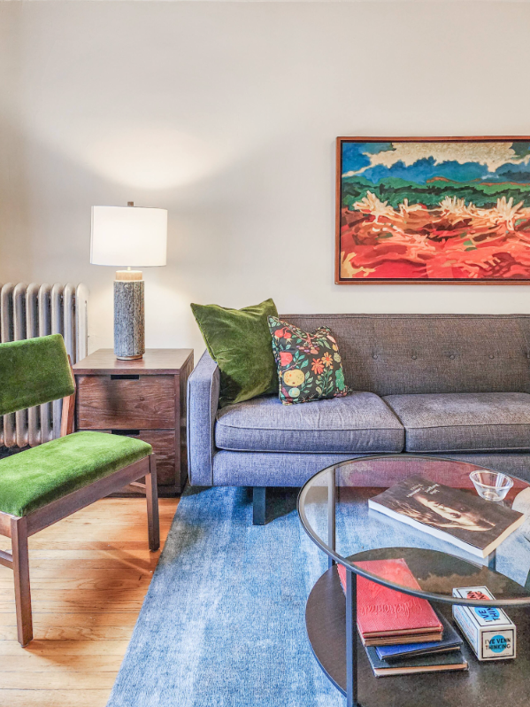A Bedder Place: Portrait detail of the living room sofa, green chair, side table, lamp, glass coffee table and colorful artwork.