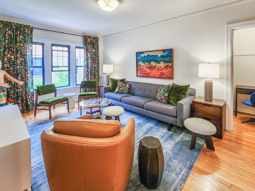 A Bedder Place: Living room facing the windows, with the caramel armchair in the foreground and gray sofa to the right.
