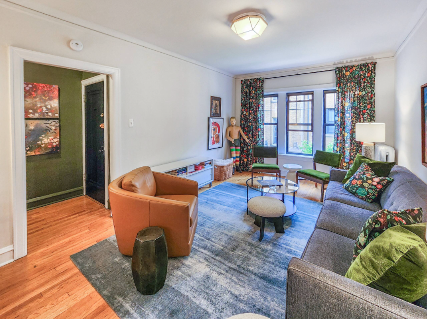 A Bedder Place: Reverse-angle living room view toward the windows, showing the caramel armchair, green chairs and sofa.