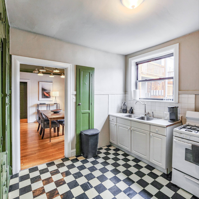 A Bedder Place: Kitchen with white cabinetry, sink, gas stove, checkerboard floor and a doorway to the dining room.
