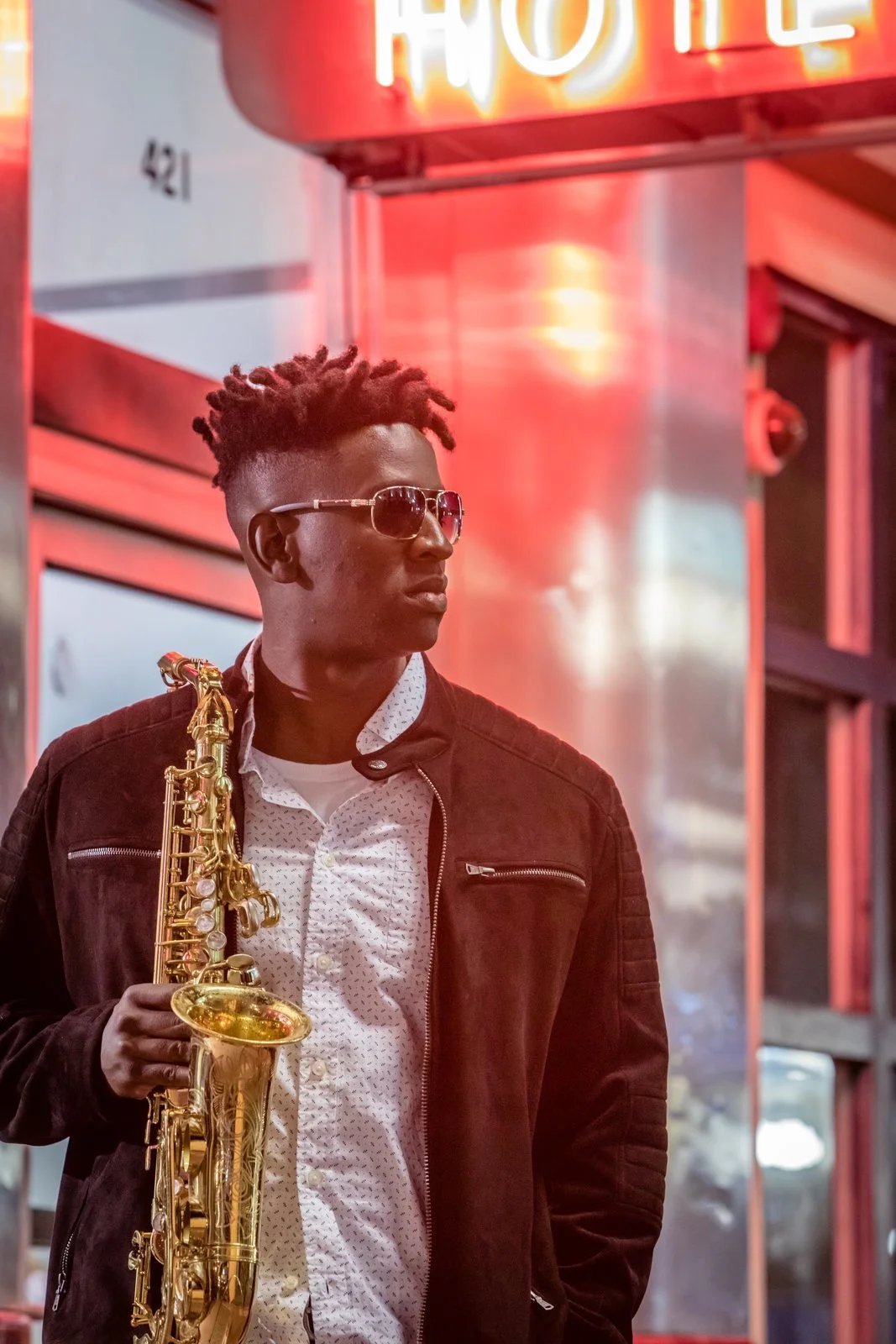 Isaac Edwards with his saxophone under neon hotel lights