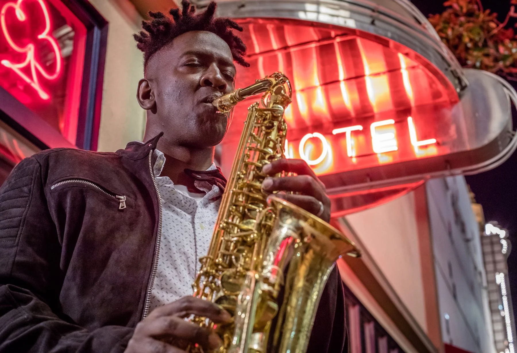 Isaac Edwards playing sax in front of a neon hotel sign