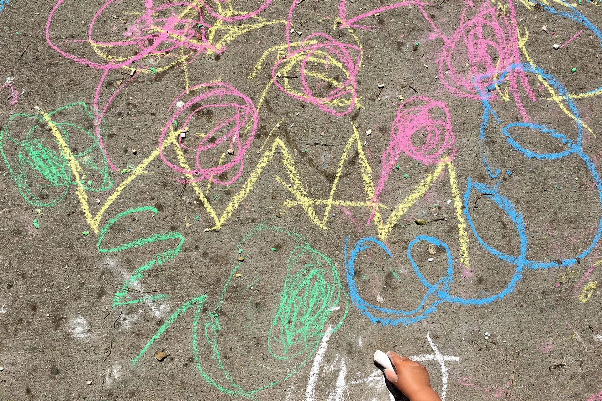 Toddler chalk scribbles in bright colors on a driveway