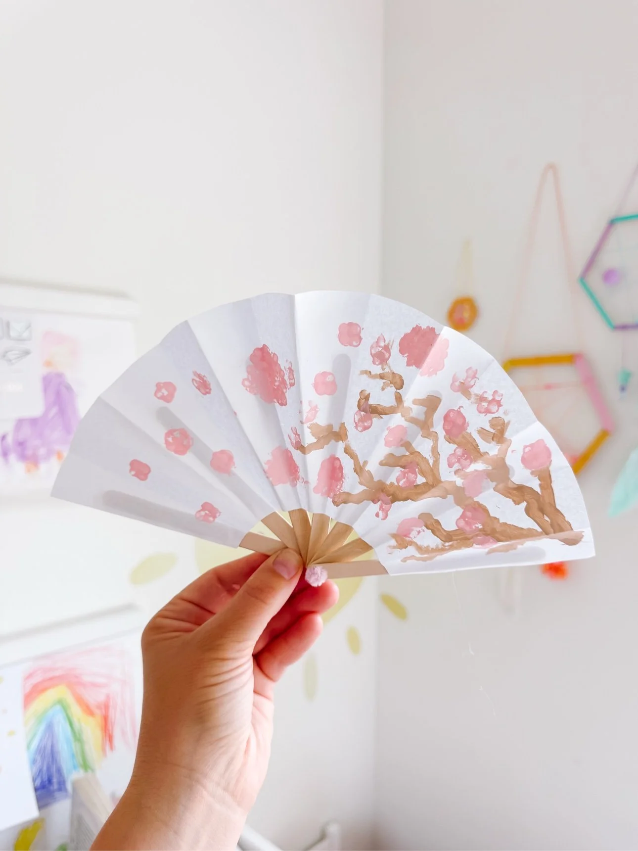 Hand holding a finished DIY paper fan painted with pink cherry blossoms