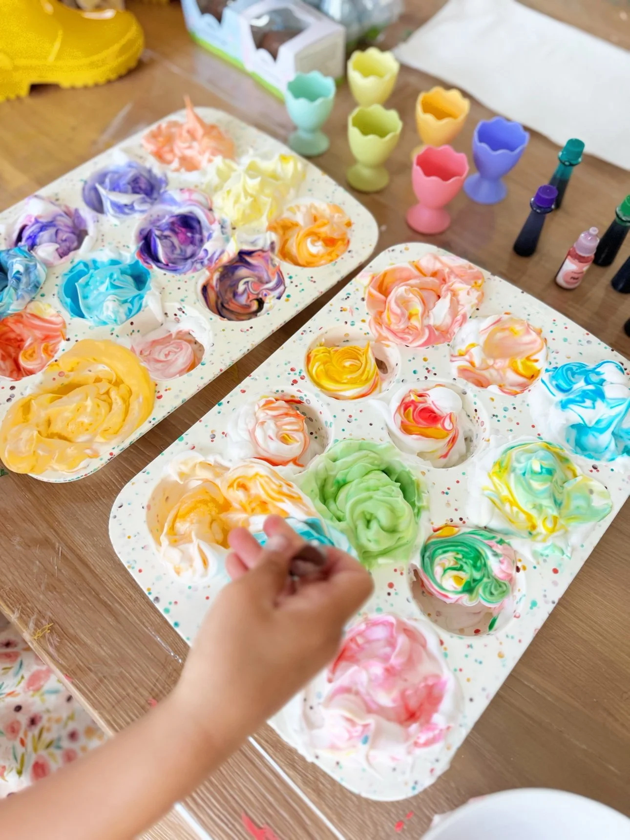 Muffin tins filled with swirled rainbow shaving foam for dyeing Easter eggs
