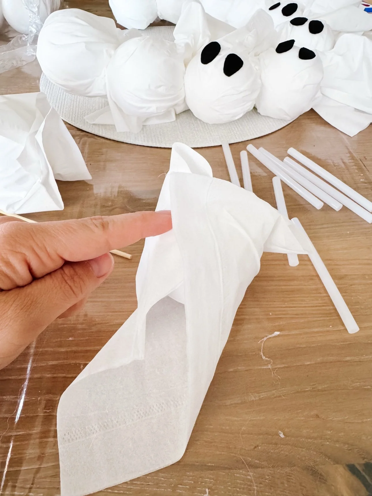 Hand gathering a white tissue around a foam ball to form a ghost head
