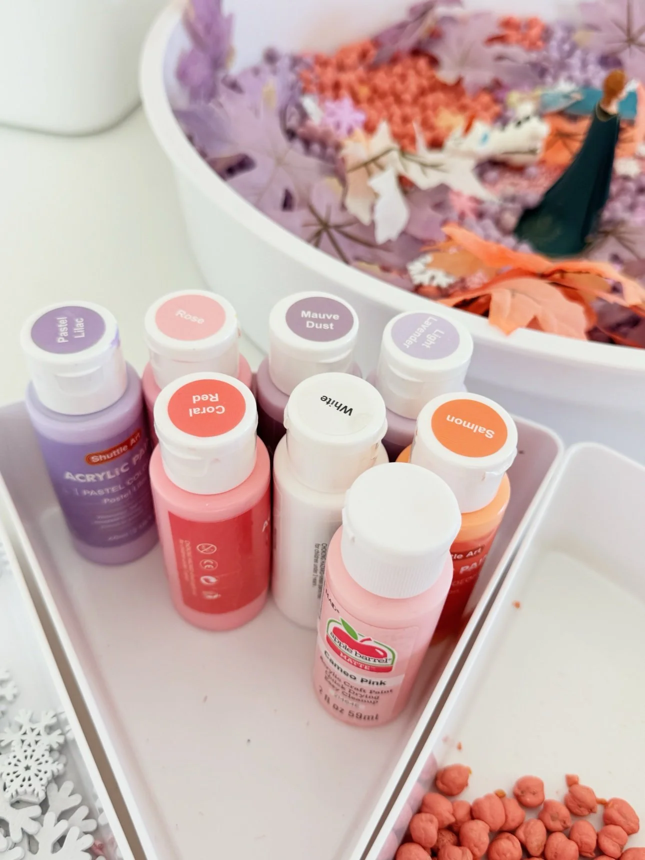 Child's hands playing in the fall frozen sensory bin with Anna, Elsa, and Olaf figurines among the pastel fillers