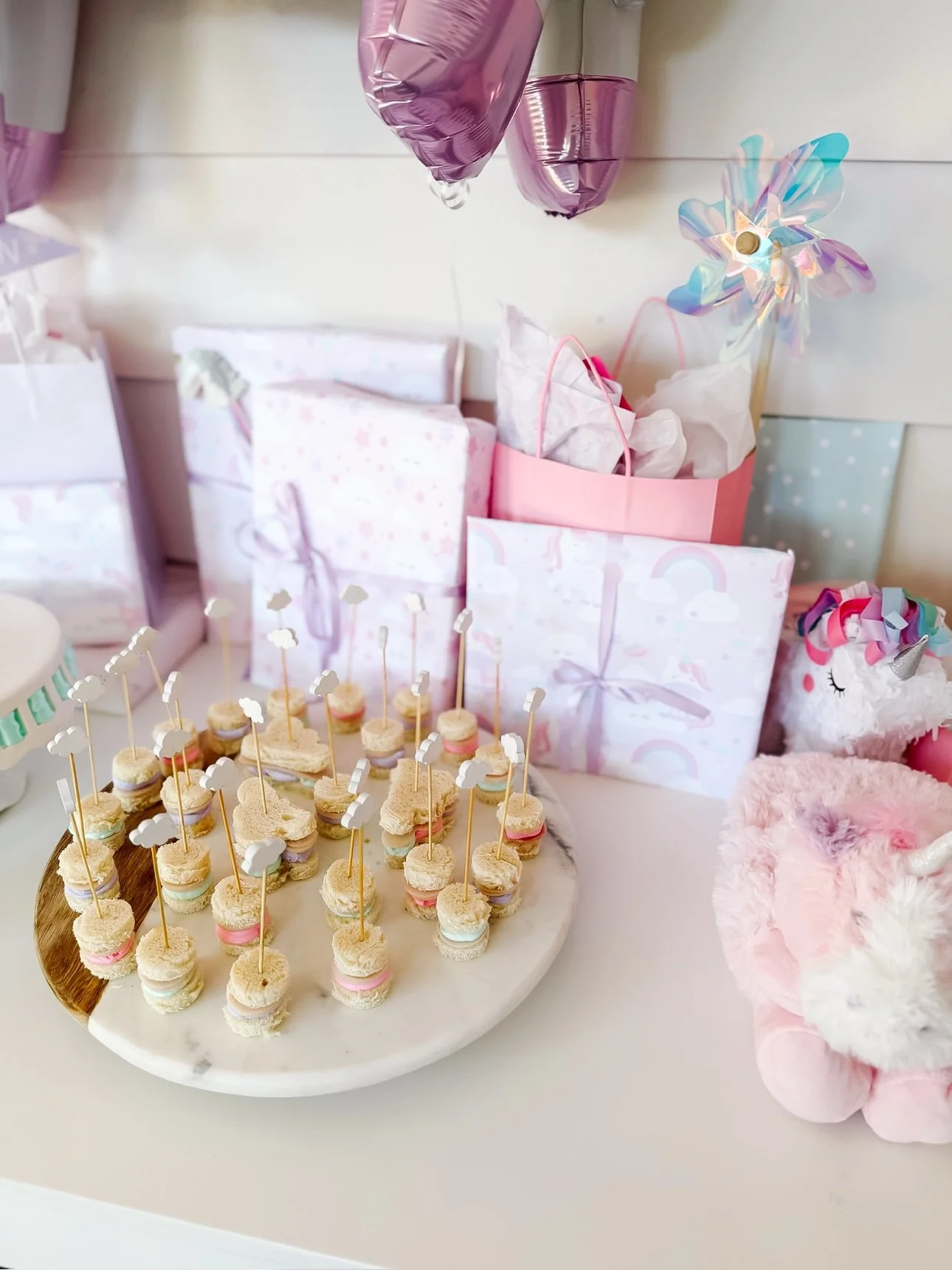 Mini sandwich stacks with cloud picks on a marble board at a unicorn party