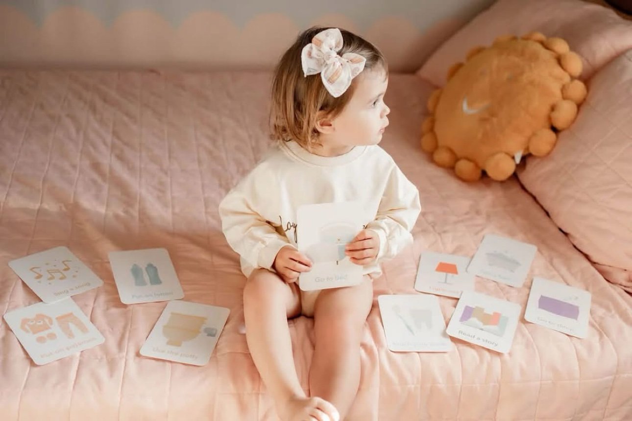 Toddler sitting on a bed looking at bedtime routine cards during wind-down