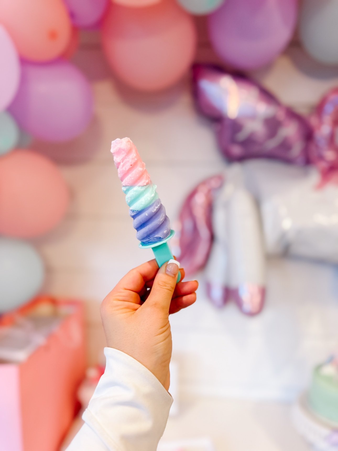 Hand holding a pastel unicorn horn frozen yogurt pop at the party