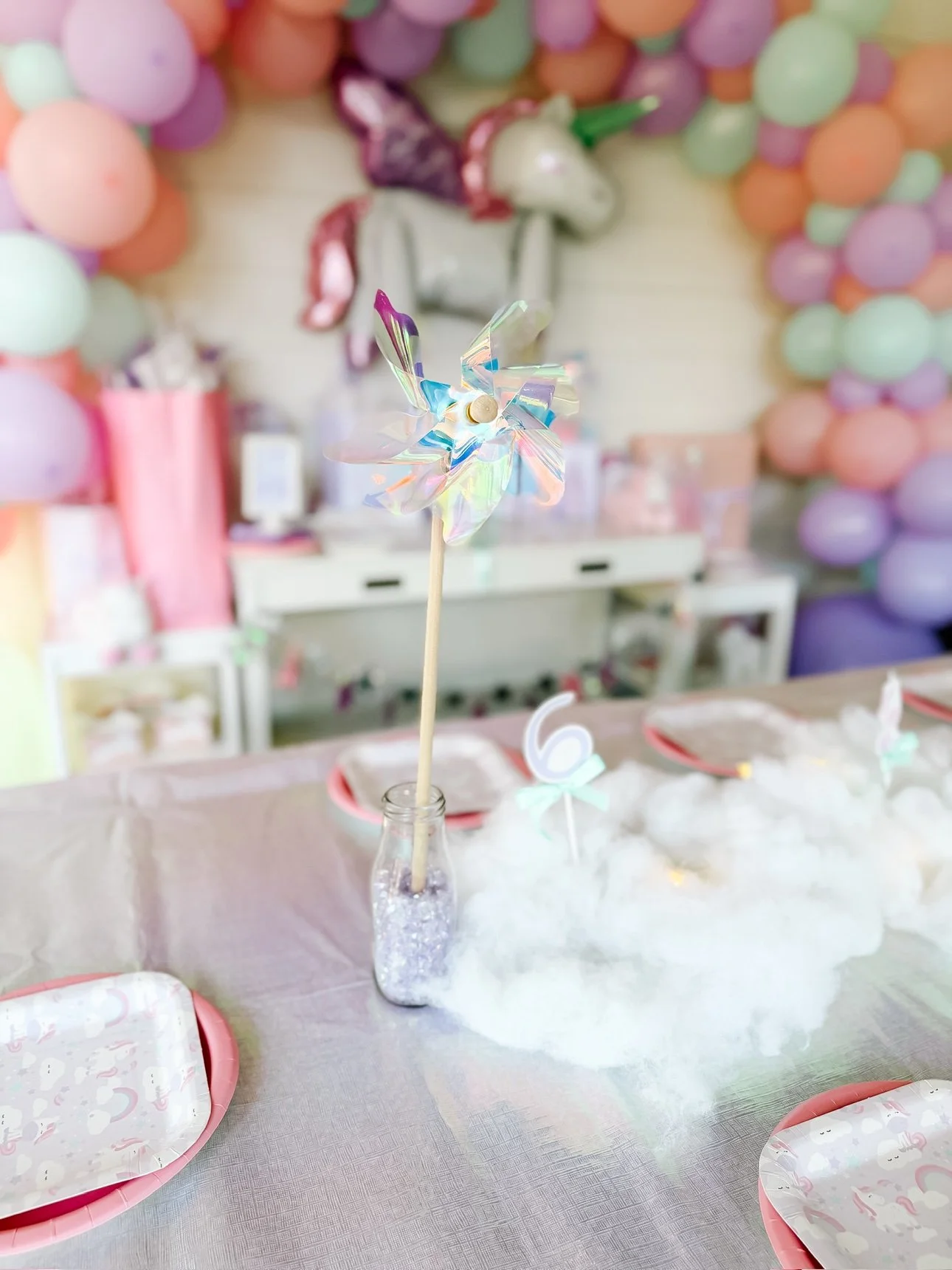 Iridescent pinwheel centerpiece on unicorn party table with balloon arch behind