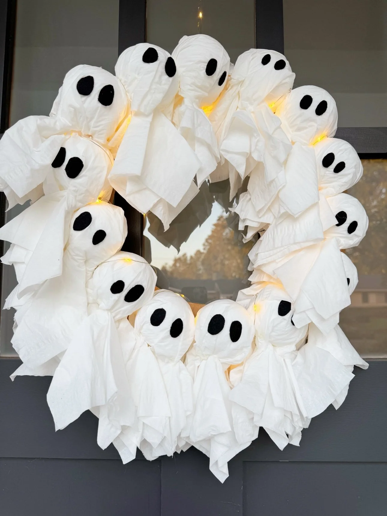 Finished light-up ghost wreath made of tissue ghosts hanging on a front door at dusk
