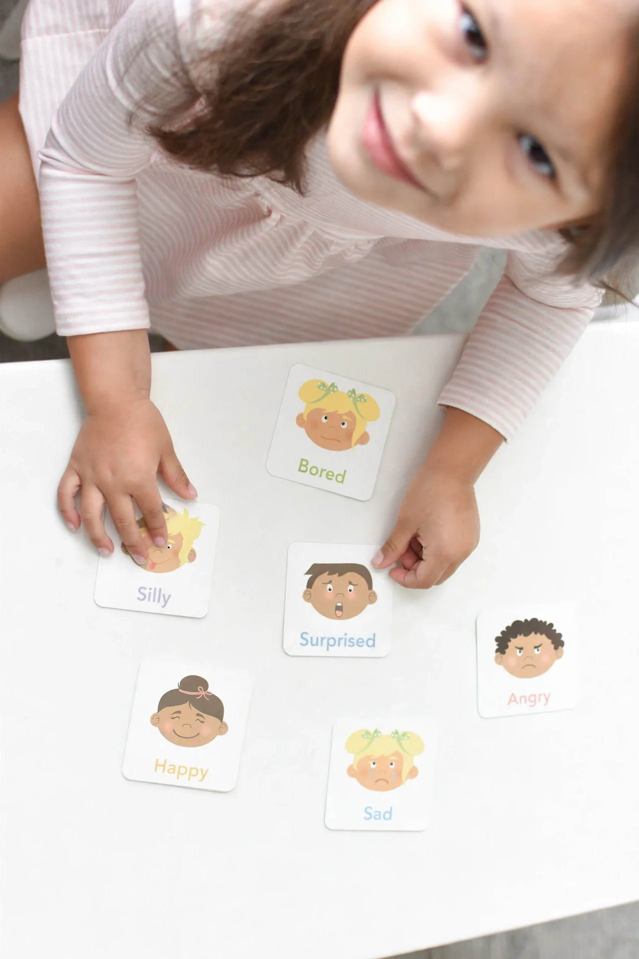 Child's hands playing an emotions card matching game on a white table