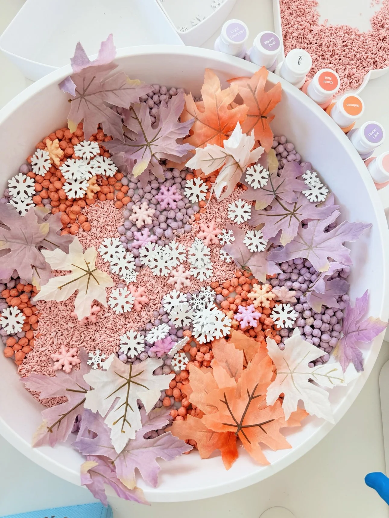 Fall frozen sensory bin: pastel dyed chickpeas, pink rice, faux fall leaves, snowflakes, and Frozen figurines in a white bowl