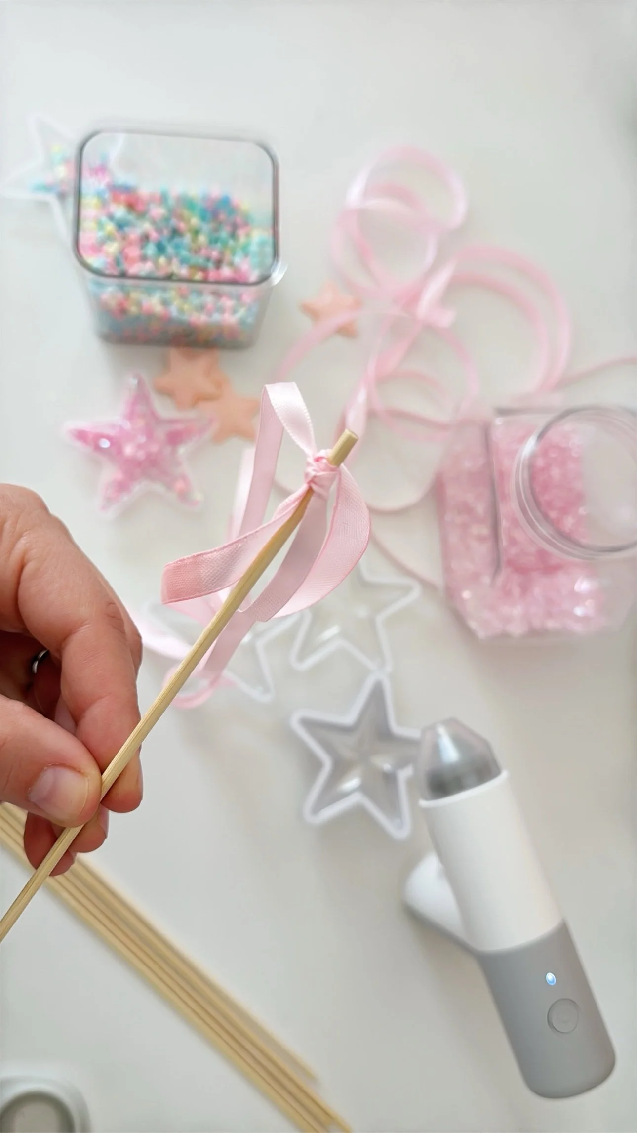 Tying pink satin ribbon streamers onto a shaker wand dowel