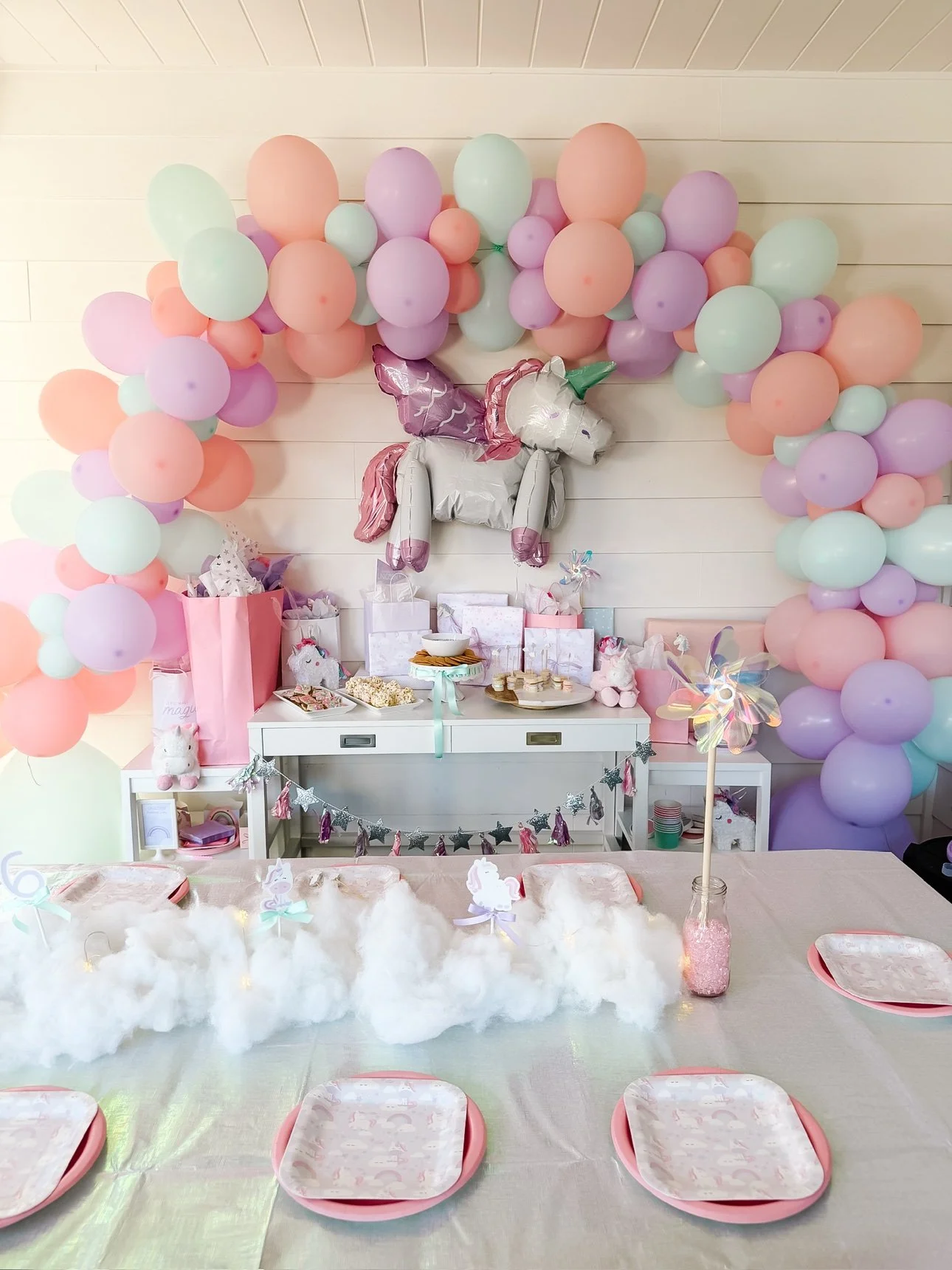 Unicorn dessert table with balloon arch, cake, cupcakes, cookies and pastel treats
