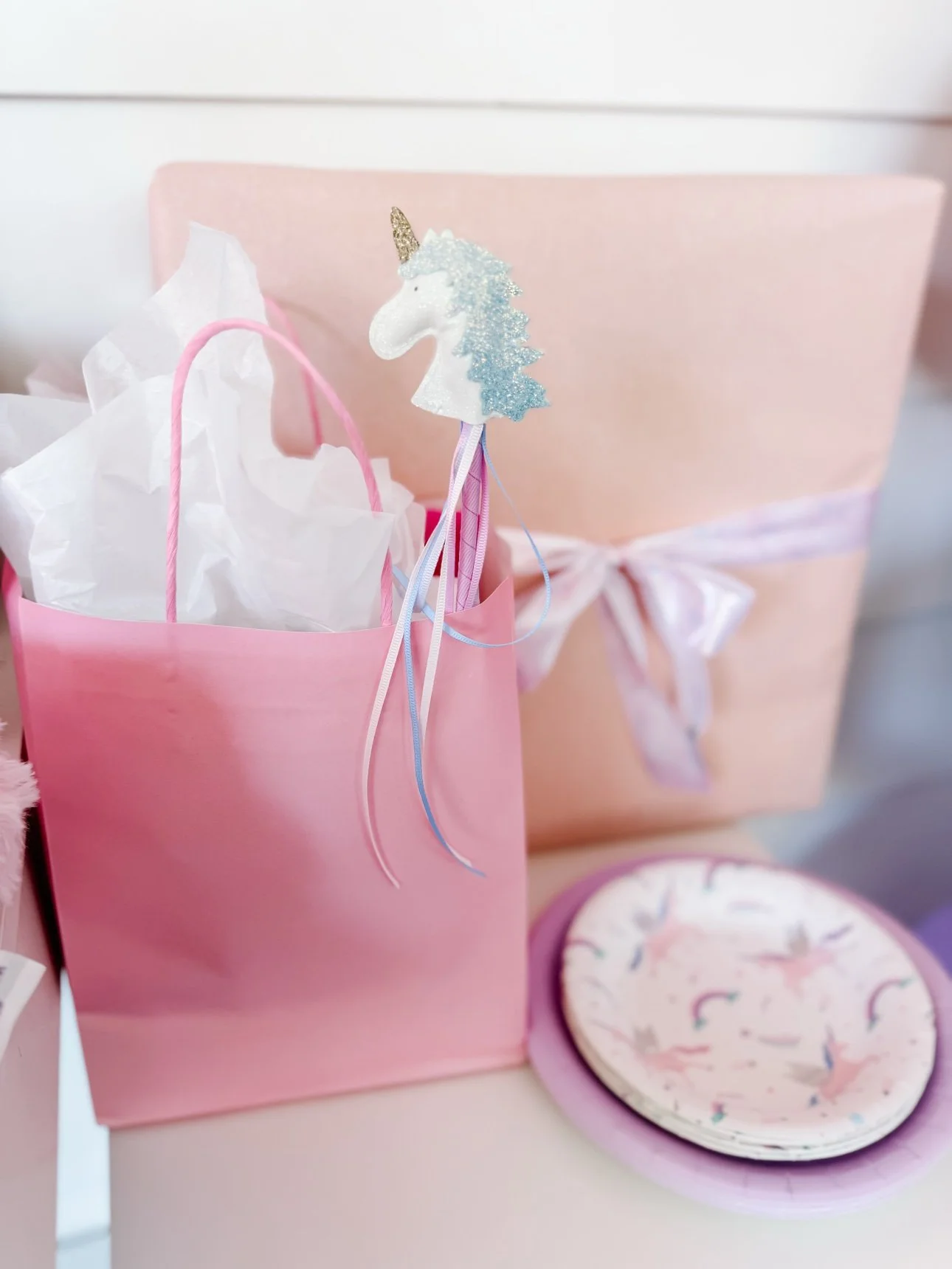 Pink unicorn party gift bag with ribbon wand, wrapped gift and unicorn plates