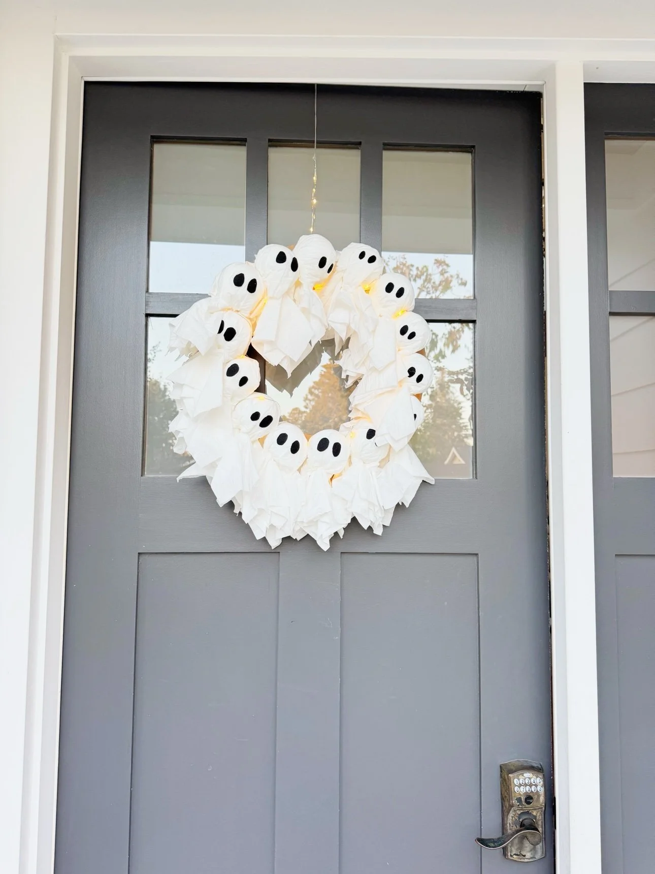 Ghost wreath hanging on a dark front door in daylight