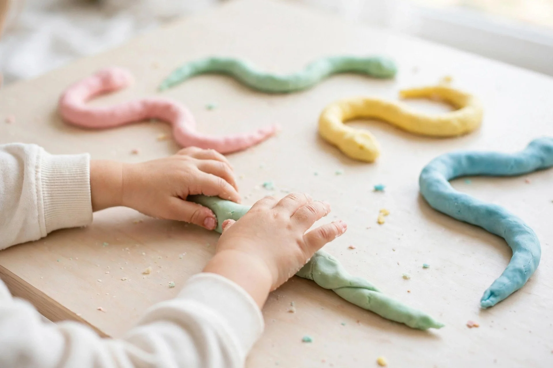 Small hands rolling colorful playdough snakes on a table
