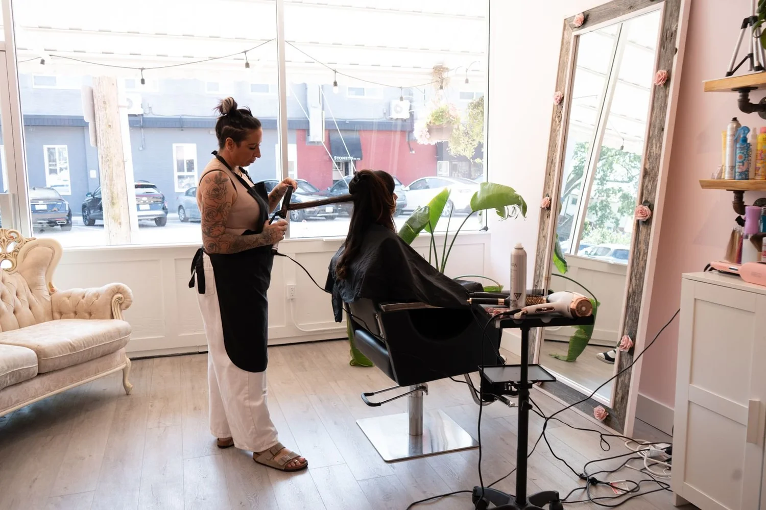 Stylist blow drying a client by the front window at Dollface