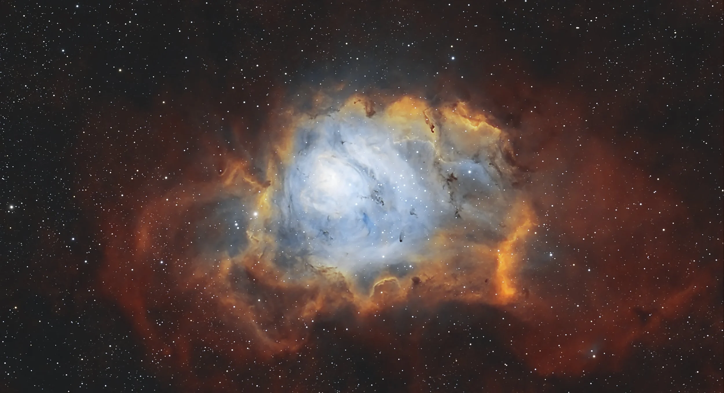 The Lagoon Nebula glowing red and blue around dark dust lanes within a dense field of stars.