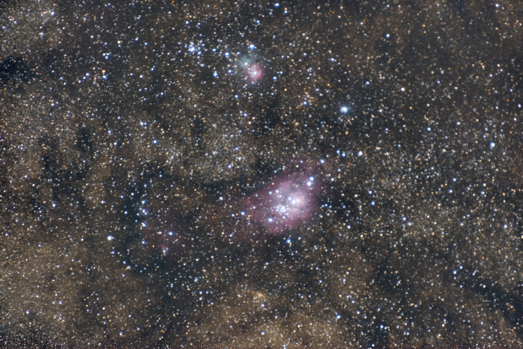 The Lagoon and Trifid nebulae appearing as small pink regions in a dense star field, photographed with a Nikon D810 at 400 mm.