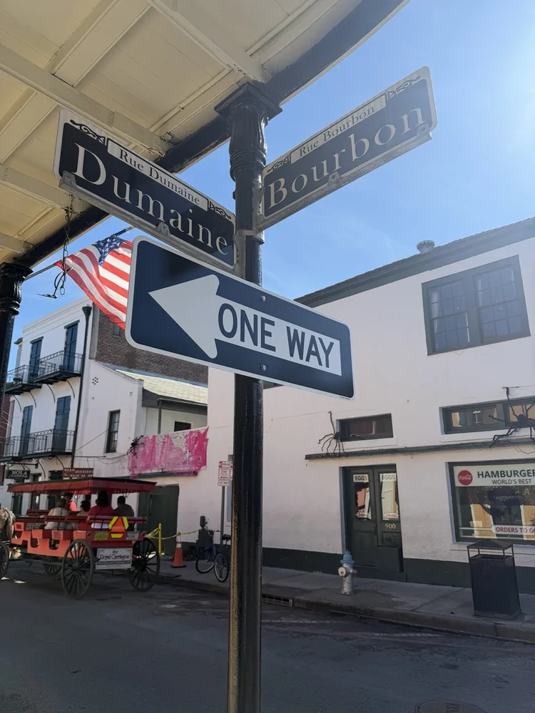 Rue Dumaine and Rue Bourbon street signs with a carriage at the French Quarter corner