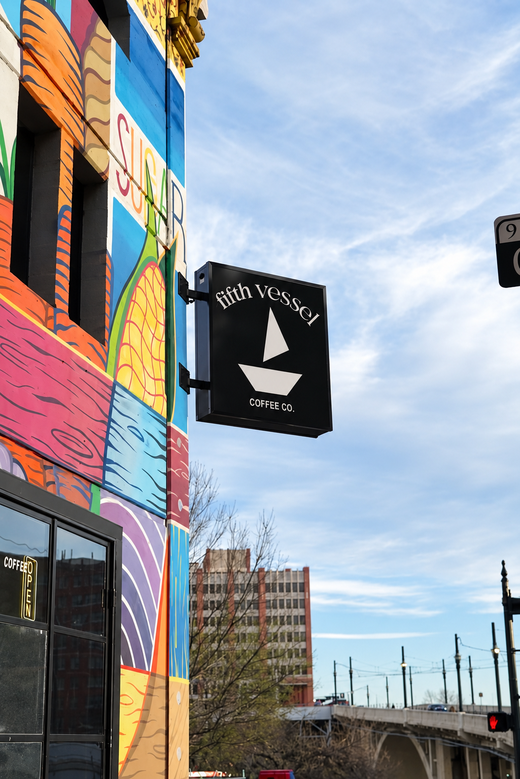 The Fifth Vessel sign against the colorful Produce Row mural