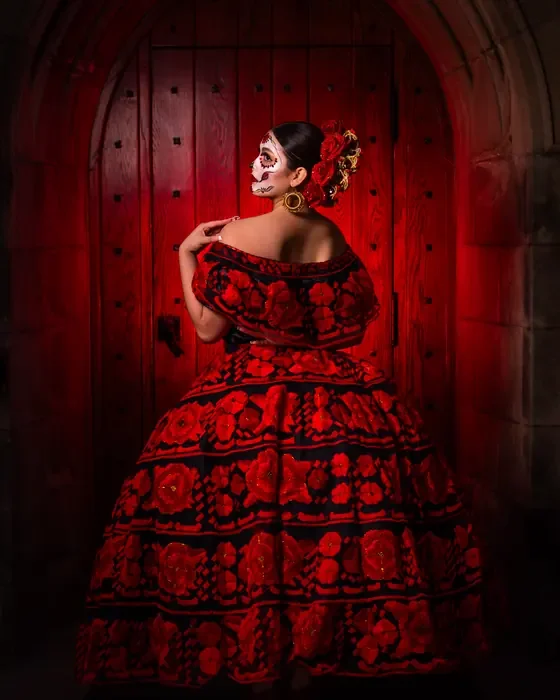 Full-length Catrina in a red embroidered dress posing before red wooden doors
