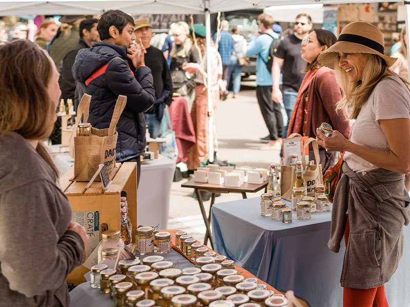 Local makers displaying handmade goods at LoHi Spring BAZAAR with shoppers browsing