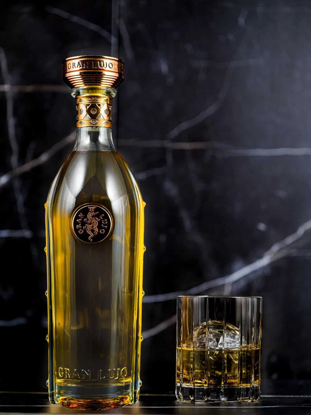Gran Lujo bottle and tumbler against dark marble