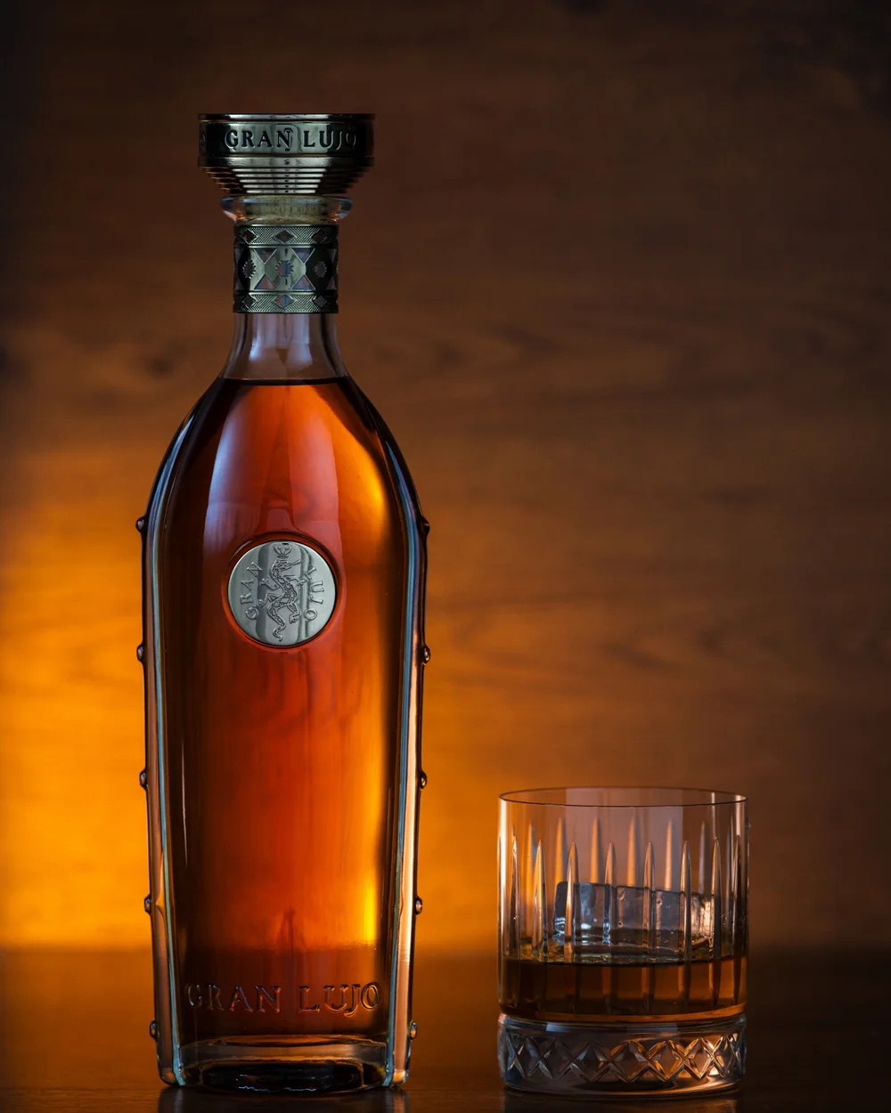 Gran Lujo bottle and cut-glass tumbler lit against a warm amber background