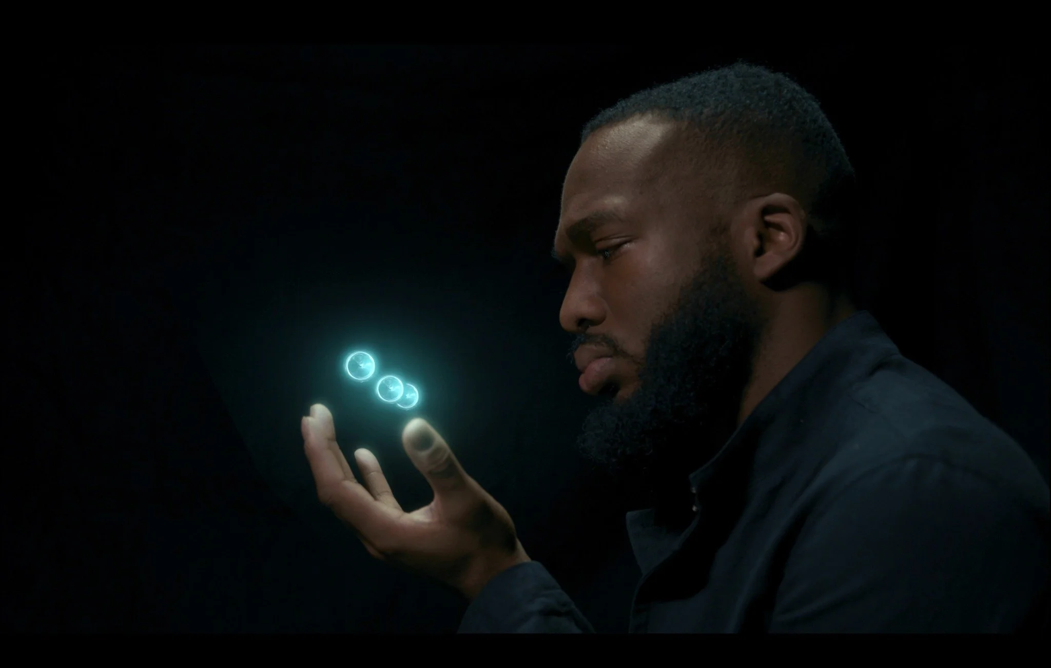 Nate Wright in profile against a black background, holding glowing blue orbs