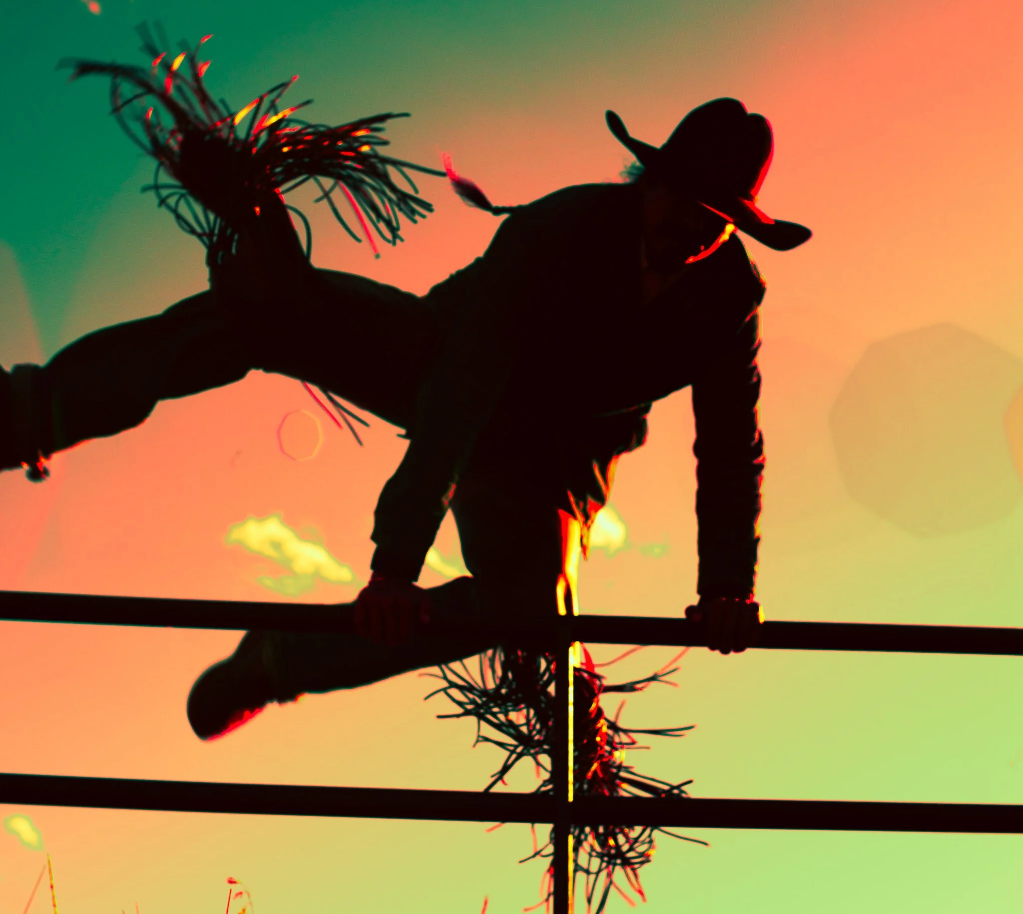 A cowboy vaulting a fence against vivid orange and green light