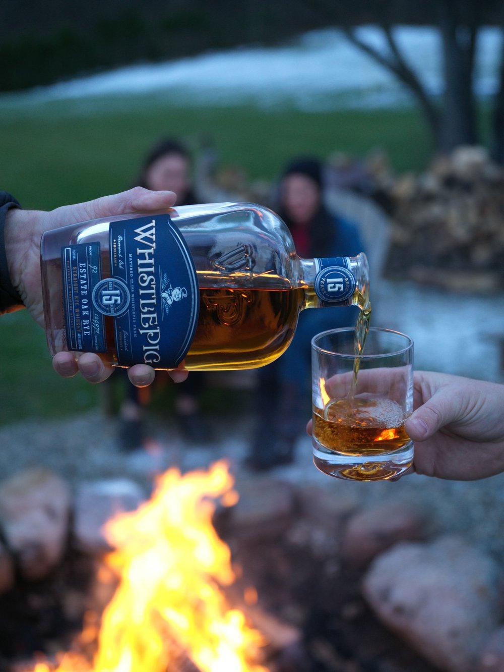 WhistlePig whiskey poured into a glass beside a campfire