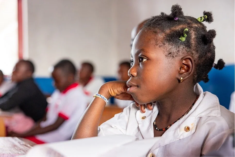 Young student rests her chin on her hand while listening in class, with other students seated behind her.