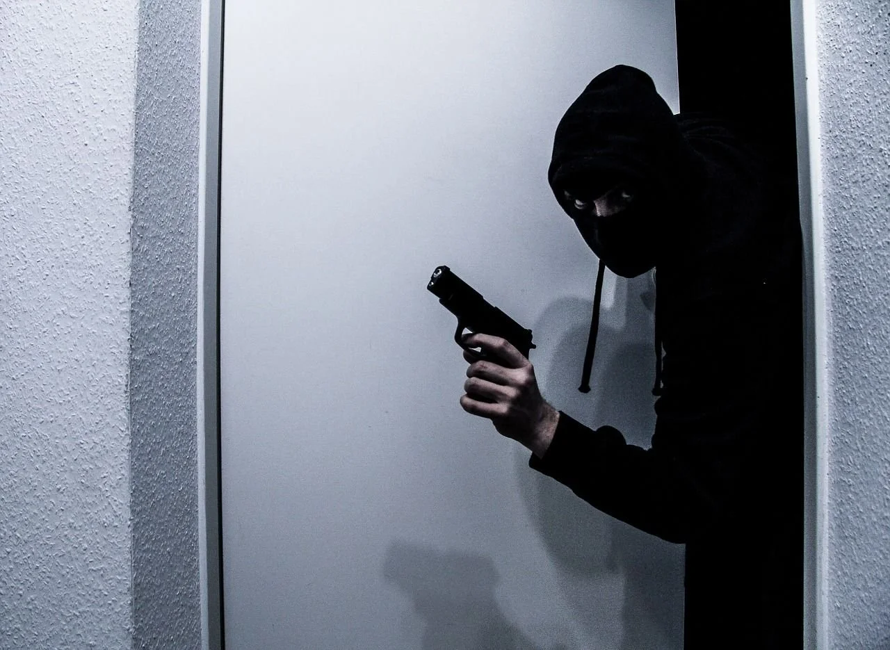 A masked intruder with a gun in a dark hallway