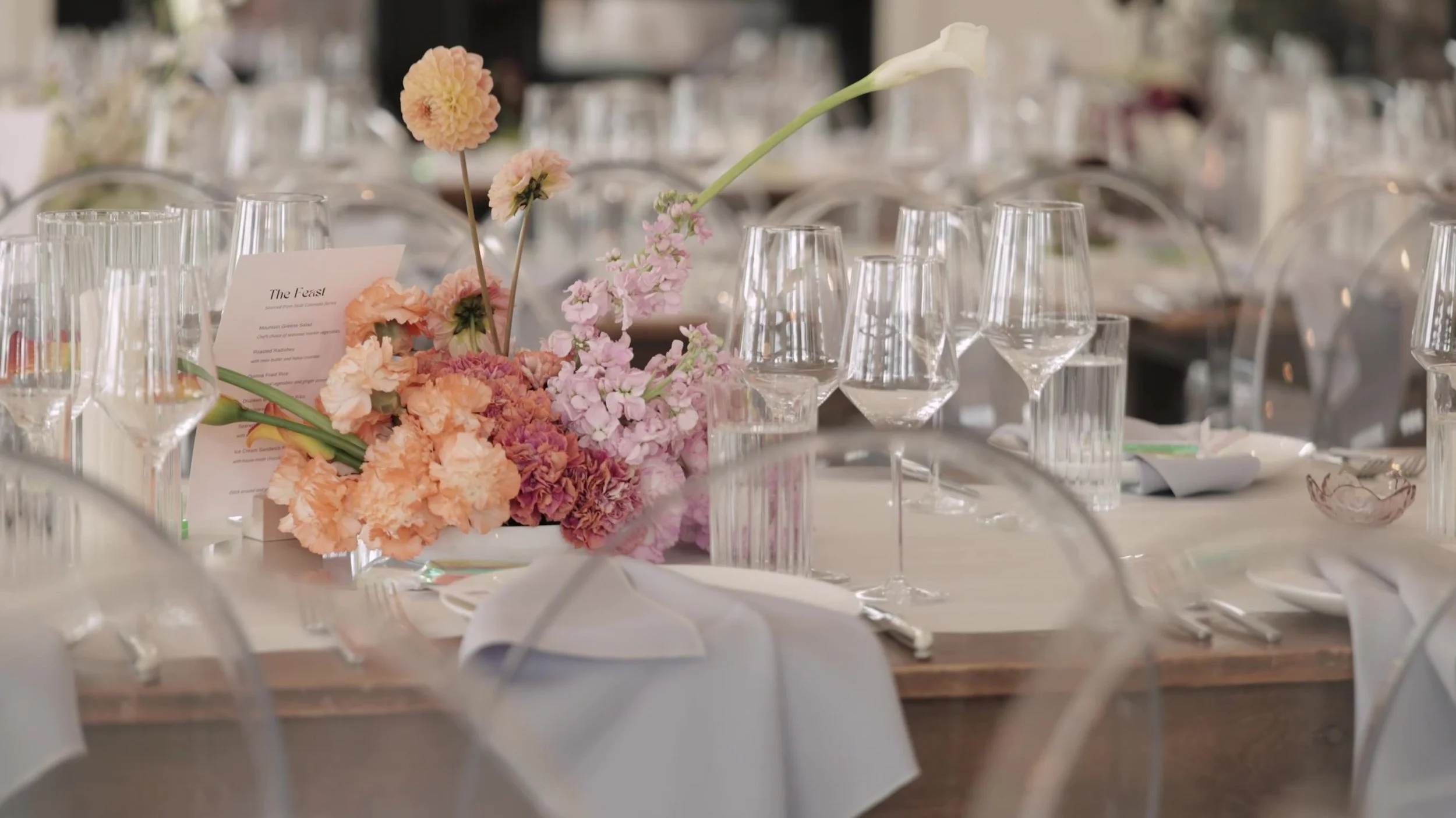 Reception table at Northstar Gatherings with peach and pink florals, glassware, and ghost chairs in Idaho Springs, Colorado