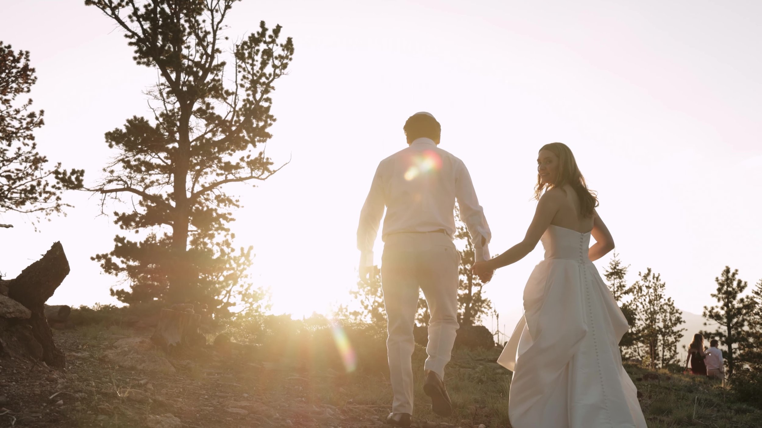 Bride and groom walking into sunset light between pines at Northstar Gatherings in Idaho Springs, Colorado