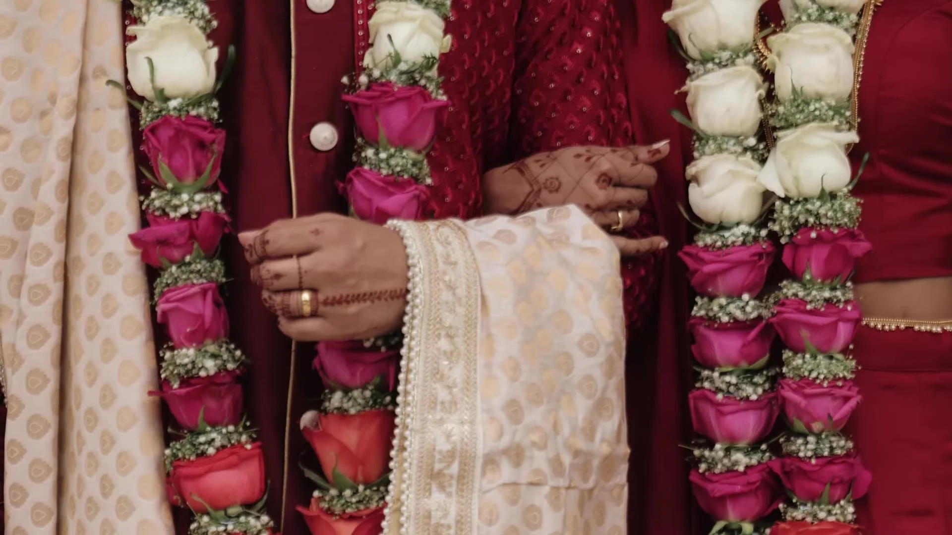 Close up of Bhavim and Mala's red sherwani and lehenga with white and pink rose varmala and mehndi hands at The Terrace Club