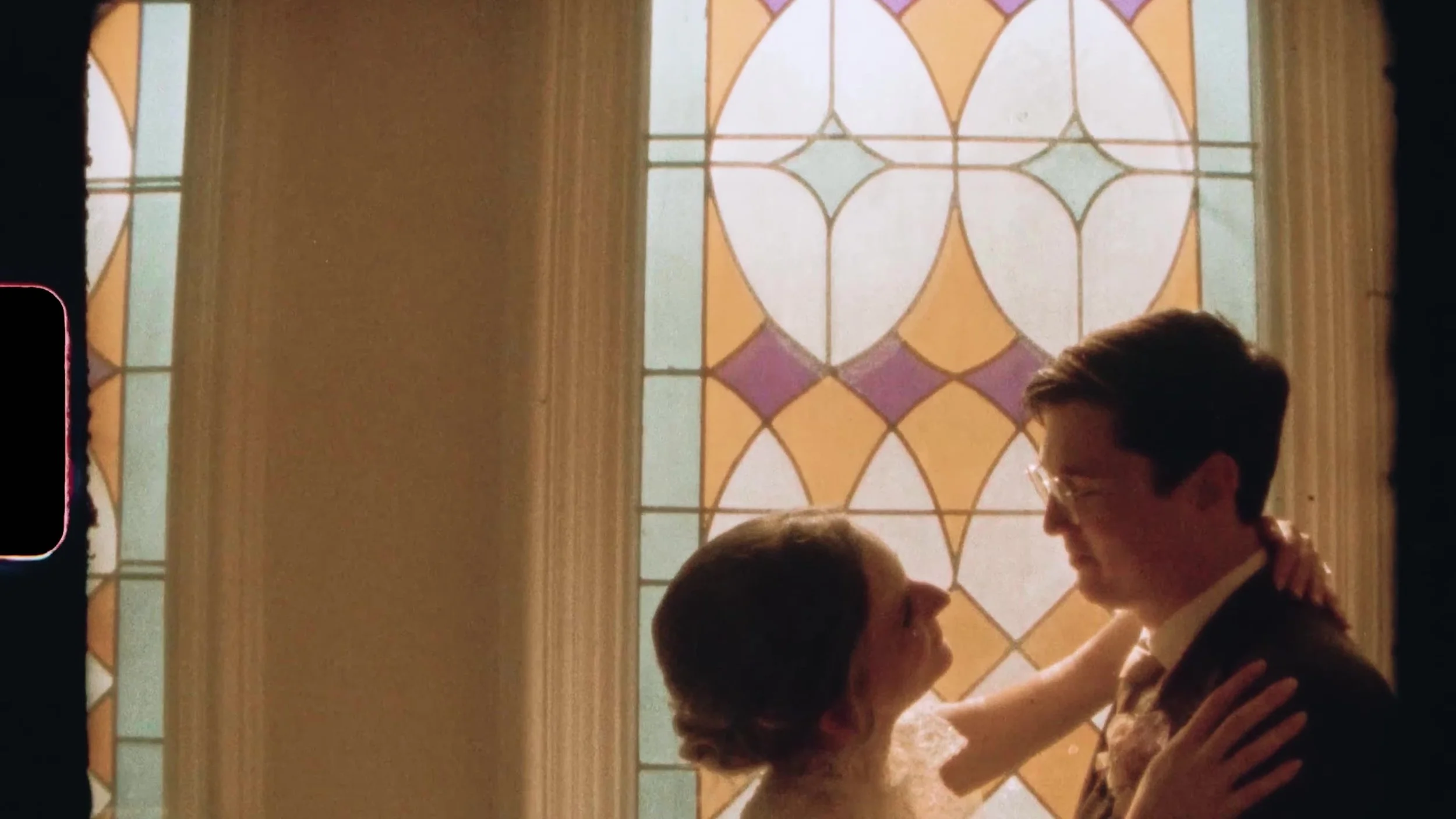 Tight film frame of bride and groom face to face by a stained glass window at Nouveau Antique Art Venue in Houston, Texas, sprocket edge visible