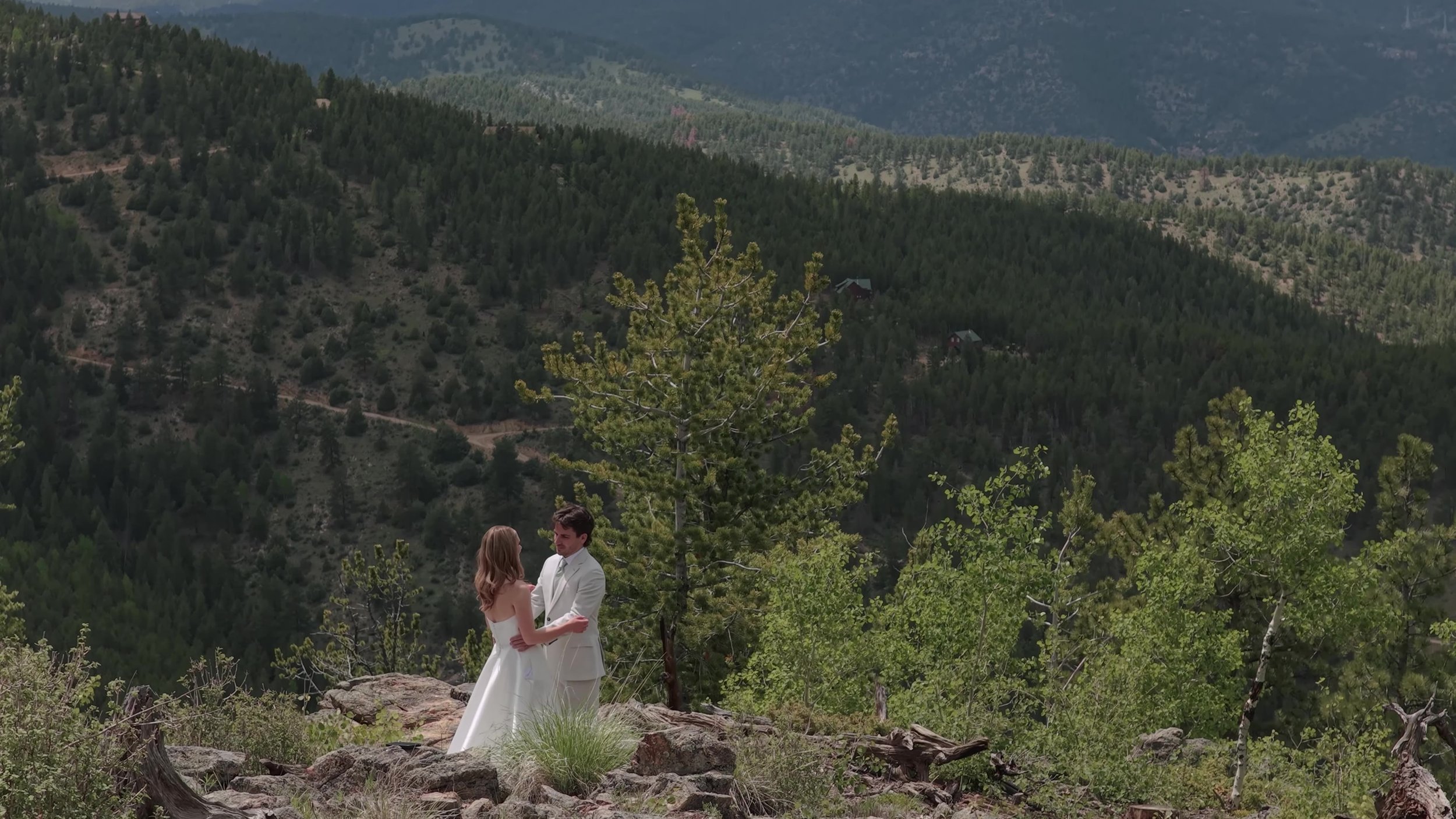 Couple together on a hillside clearing with aspen, pine, and a valley behind them at Northstar Gatherings in Idaho Springs, Colorado