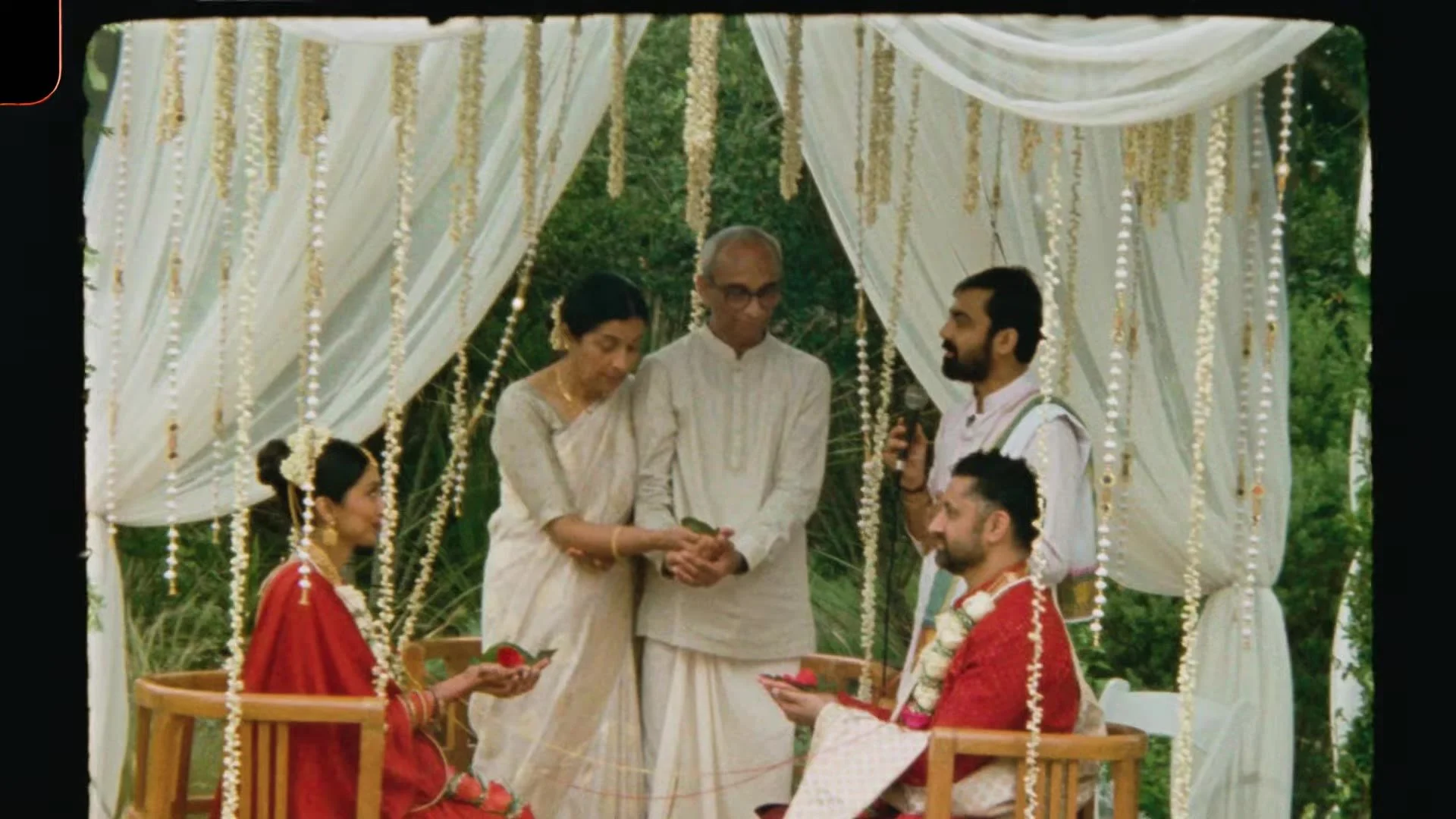 Bhavim and Mala seated under the mandap while family performs a ritual with a priest at The Terrace Club Indian wedding in Austin