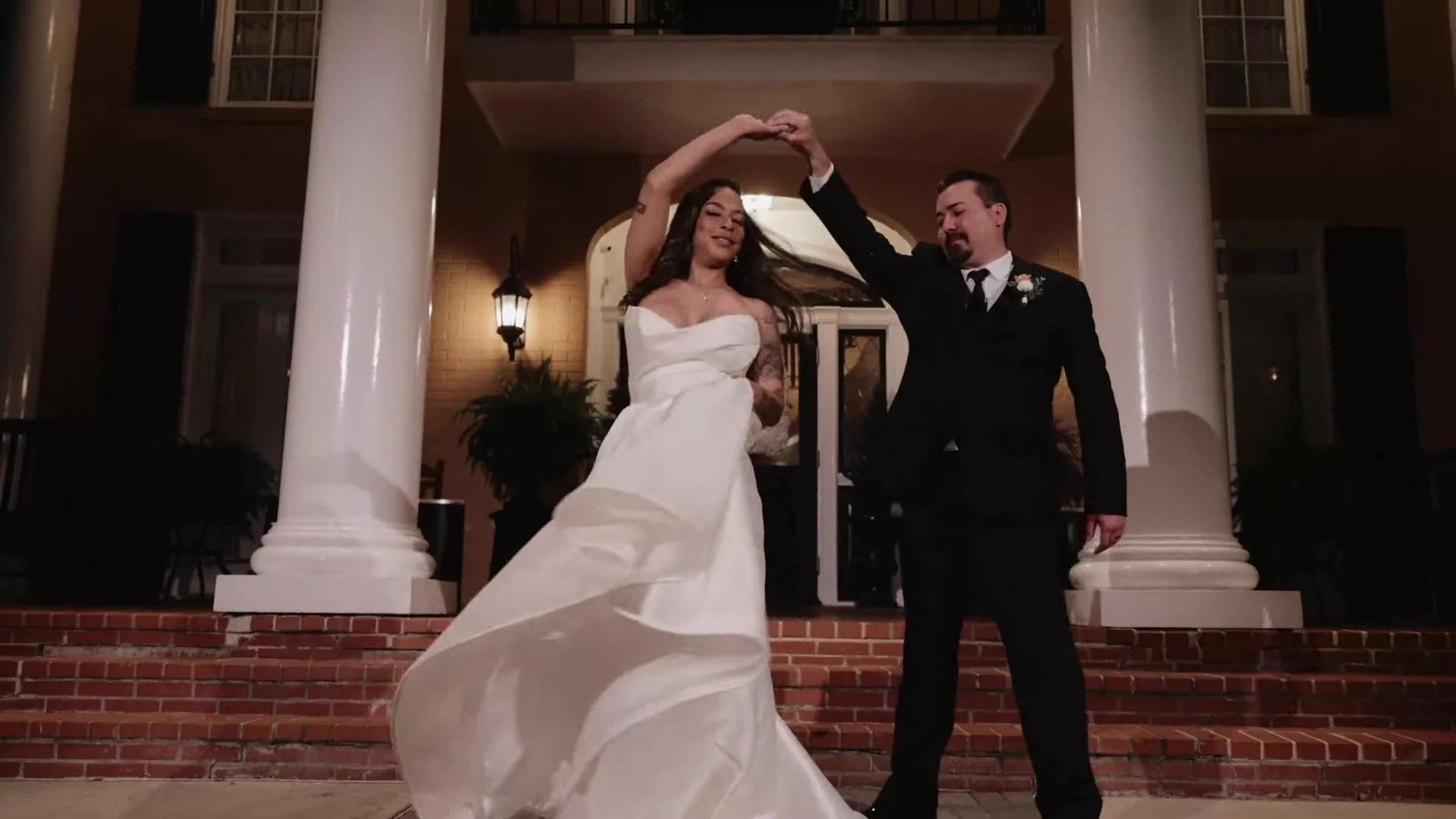 Blair and Gustavo twirling on the brick steps of Southern Oaks Plantation between white columns at night